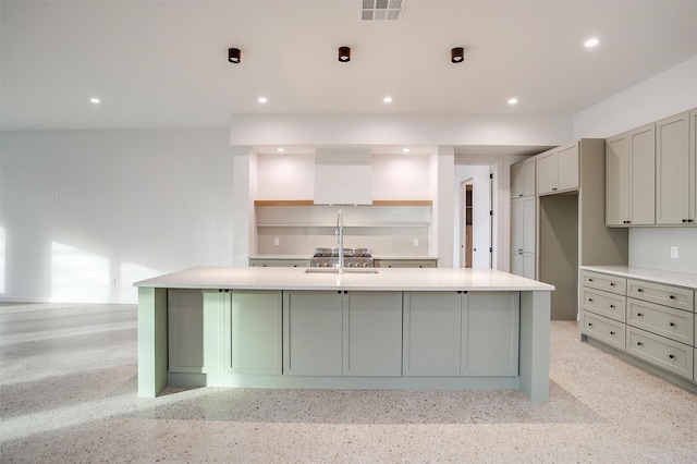 kitchen with wall chimney range hood, gray cabinets, sink, and a large island with sink