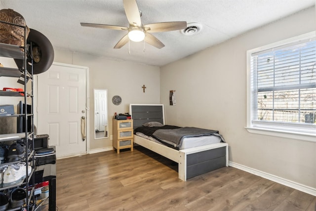 bedroom featuring a textured ceiling, ceiling fan, dark hardwood / wood-style flooring, and multiple windows