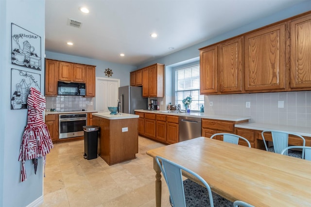 kitchen with decorative backsplash, brown cabinetry, visible vents, a center island, and black appliances