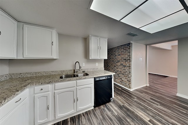 kitchen featuring light stone countertops, brick wall, white cabinets, black dishwasher, and sink