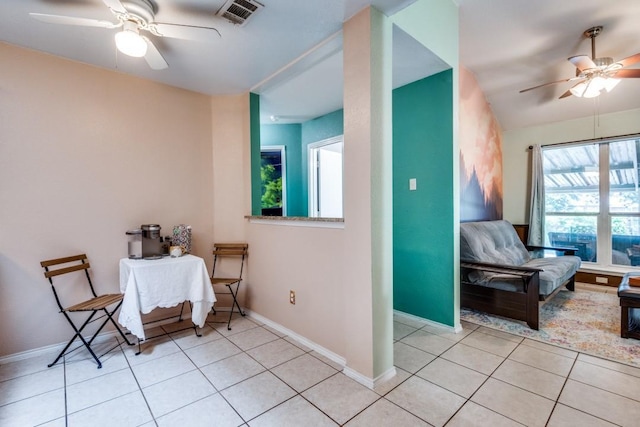 living area with light tile patterned floors, ceiling fan, visible vents, and baseboards