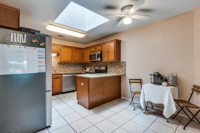 kitchen with a skylight, brown cabinets, stainless steel appliances, light countertops, and backsplash