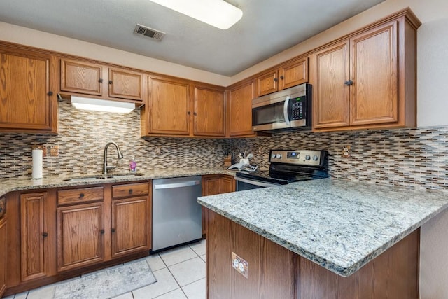 kitchen with light stone counters, brown cabinets, stainless steel appliances, visible vents, and a sink