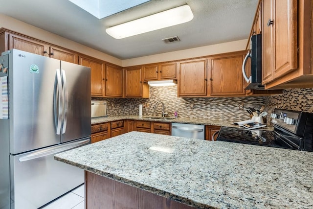 kitchen with light stone counters, visible vents, appliances with stainless steel finishes, brown cabinetry, and a peninsula