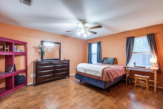 bedroom featuring baseboards, multiple windows, visible vents, and wood finished floors