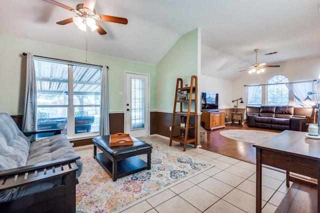 living room with lofted ceiling, ceiling fan, light tile patterned flooring, visible vents, and wainscoting