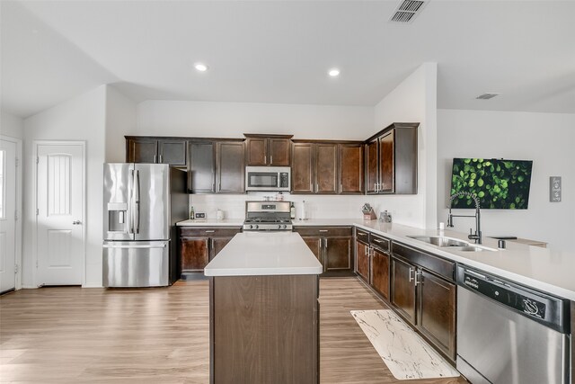 kitchen featuring appliances with stainless steel finishes, sink, light wood-type flooring, kitchen peninsula, and vaulted ceiling