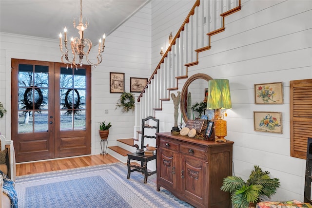 entrance foyer featuring hardwood / wood-style floors, french doors, wood walls, a chandelier, and crown molding