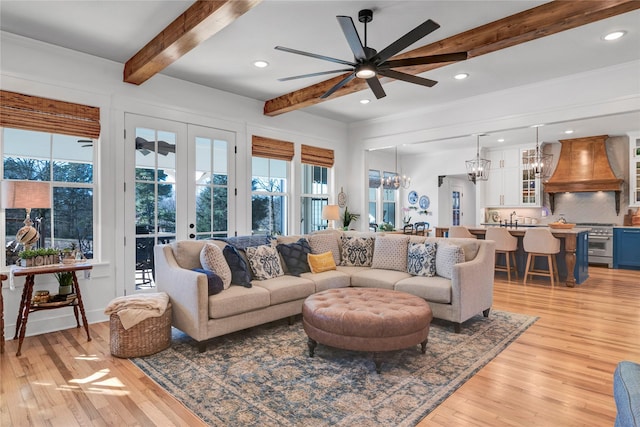 living room with ceiling fan with notable chandelier, french doors, beamed ceiling, sink, and light wood-type flooring