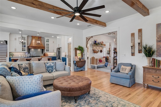 living room with beam ceiling, ceiling fan with notable chandelier, light hardwood / wood-style floors, sink, and crown molding