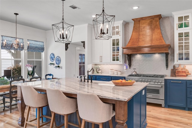 kitchen with stainless steel range, blue cabinets, custom range hood, and an island with sink