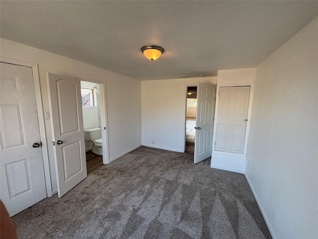 unfurnished bedroom with dark carpet, ensuite bathroom, and a textured ceiling