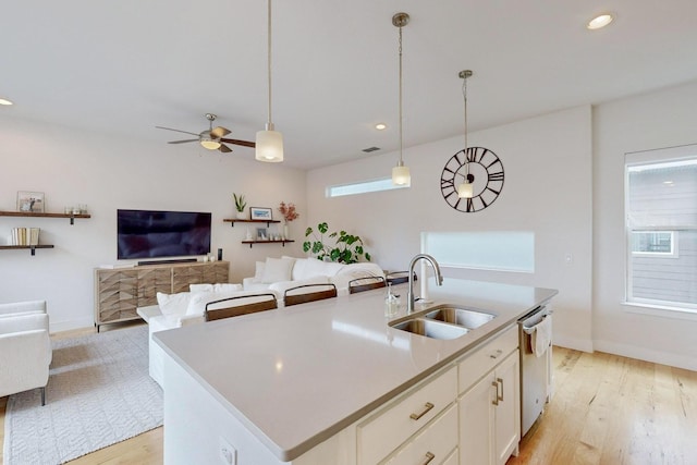 kitchen featuring stainless steel dishwasher, hanging light fixtures, sink, and a center island with sink