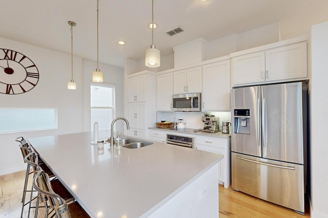 kitchen featuring a center island with sink, visible vents, a sink, appliances with stainless steel finishes, and white cabinetry