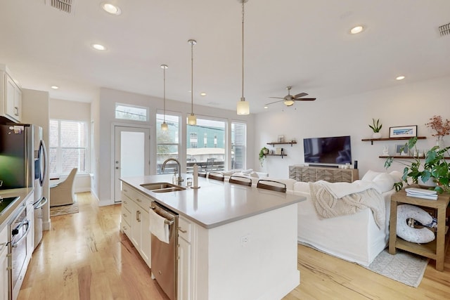 kitchen featuring pendant lighting, sink, a kitchen island with sink, stainless steel appliances, and white cabinets