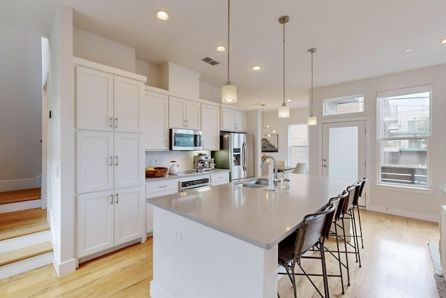 kitchen featuring white cabinetry, an island with sink, appliances with stainless steel finishes, a kitchen breakfast bar, and pendant lighting