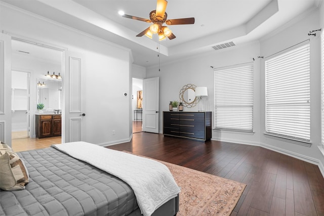 bedroom with visible vents, hardwood / wood-style flooring, ensuite bath, baseboards, and a raised ceiling