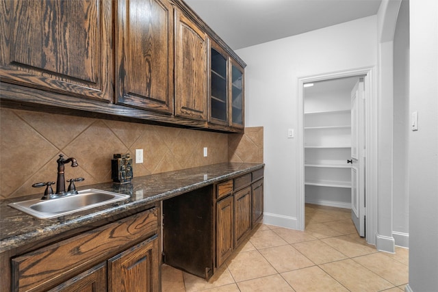 kitchen with light tile patterned floors, glass insert cabinets, backsplash, and a sink