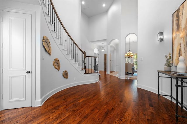 entryway featuring wood finished floors, an inviting chandelier, a high ceiling, arched walkways, and stairs