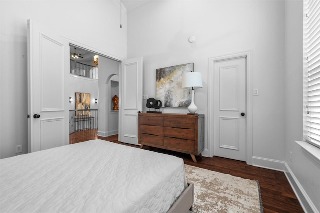 bedroom with dark wood-type flooring, baseboards, multiple windows, a towering ceiling, and arched walkways