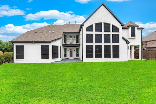 rear view of property with a patio, a balcony, fence, a yard, and brick siding