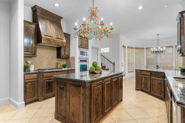 kitchen featuring premium range hood, backsplash, appliances with stainless steel finishes, light tile patterned flooring, and a chandelier