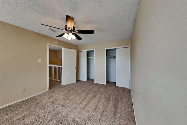 unfurnished bedroom featuring ceiling fan, multiple closets, carpet floors, and a textured ceiling