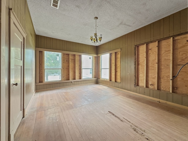 unfurnished room featuring wood-type flooring, a textured ceiling, visible vents, and an inviting chandelier