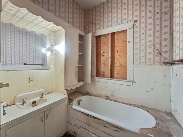 full bathroom featuring a tub, vanity, a wainscoted wall, and wallpapered walls