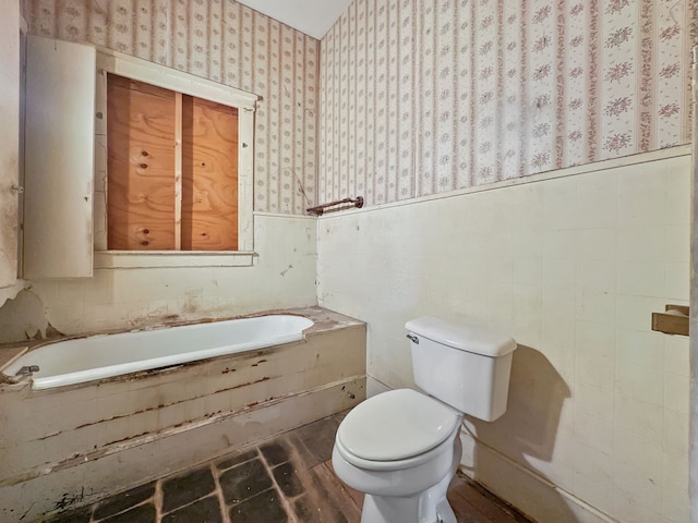 full bath with toilet, wallpapered walls, a garden tub, and a wainscoted wall