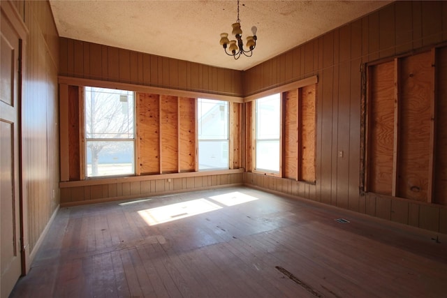 spare room featuring hardwood / wood-style flooring, a textured ceiling, a chandelier, and wooden walls