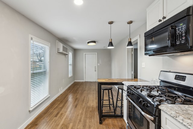 kitchen featuring an AC wall unit, white cabinets, stainless steel gas range, decorative light fixtures, and light wood-type flooring