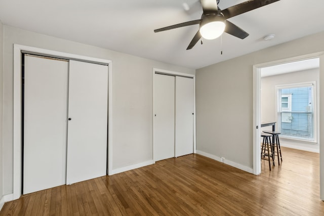 unfurnished bedroom featuring ceiling fan, wood-type flooring, and two closets