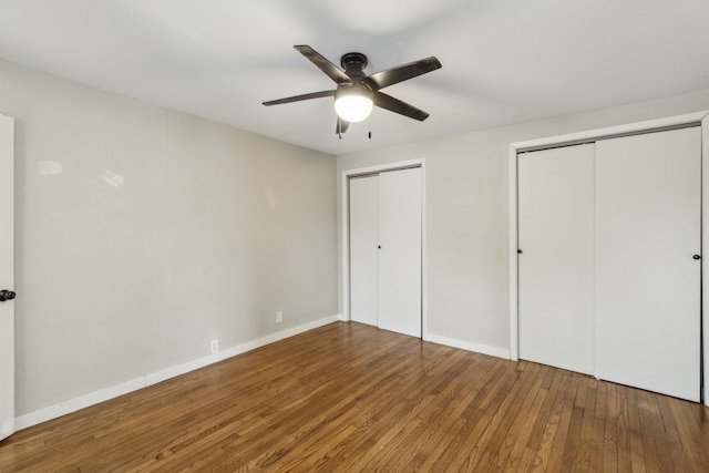 unfurnished bedroom with ceiling fan, wood-type flooring, and multiple closets