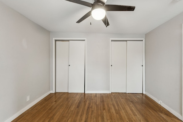 unfurnished bedroom featuring ceiling fan, multiple closets, and dark hardwood / wood-style flooring