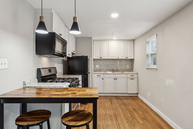 kitchen with white cabinetry, butcher block counters, black appliances, a breakfast bar, and sink