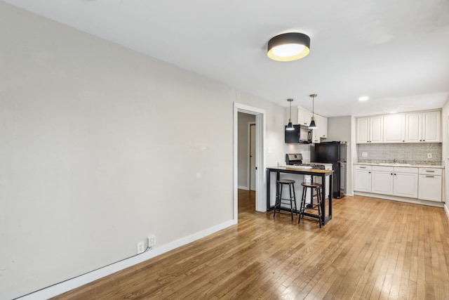 kitchen with white cabinetry, decorative backsplash, decorative light fixtures, a breakfast bar, and black appliances