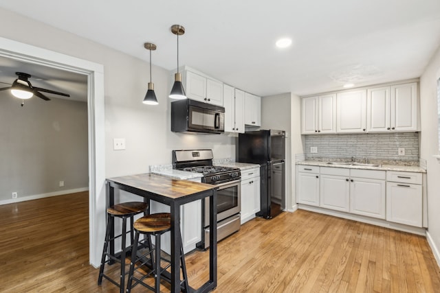 kitchen with black appliances, white cabinetry, light hardwood / wood-style floors, sink, and hanging light fixtures