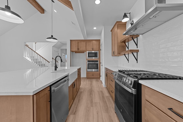 kitchen with stainless steel appliances, a sink, wall chimney range hood, light wood-type flooring, and brown cabinetry