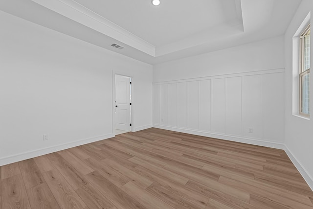 empty room with light wood-type flooring, visible vents, a tray ceiling, and baseboards