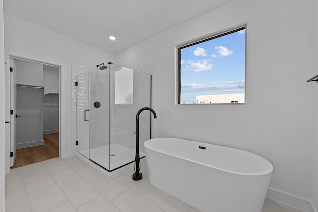 full bathroom with a stall shower, baseboards, tile patterned floors, a walk in closet, and a freestanding tub