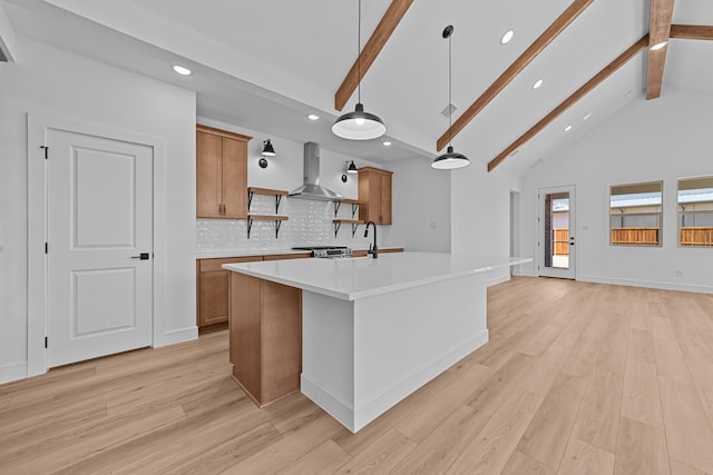 kitchen featuring light wood finished floors, wall chimney exhaust hood, brown cabinets, beamed ceiling, and light countertops