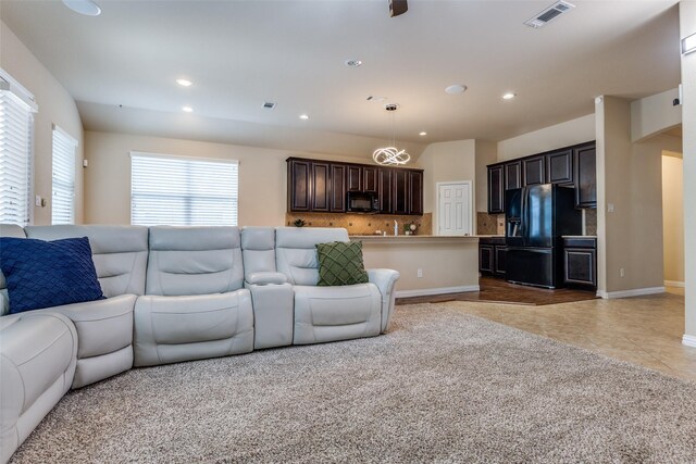 kitchen featuring decorative light fixtures, backsplash, black appliances, and a center island with sink