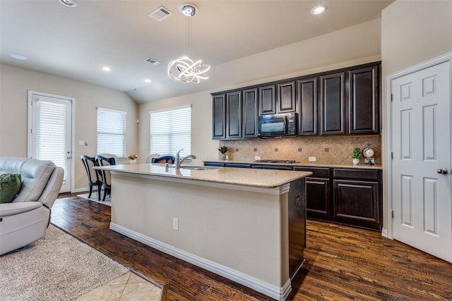 kitchen featuring decorative light fixtures, dark wood-type flooring, decorative backsplash, a center island with sink, and dark brown cabinets