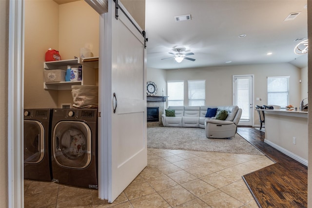 laundry room featuring ceiling fan, washing machine and dryer, light tile patterned floors, a barn door, and a tile fireplace