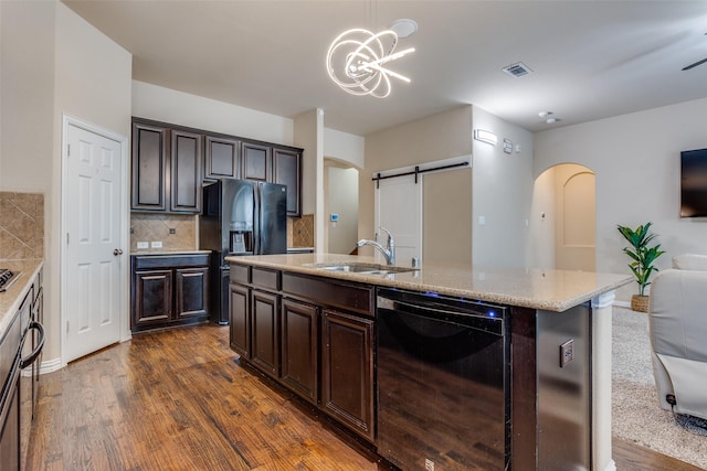 kitchen featuring black appliances, a barn door, a kitchen island with sink, dark brown cabinets, and sink