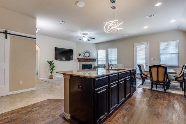 kitchen featuring pendant lighting, sink, light stone countertops, ceiling fan with notable chandelier, and a center island with sink