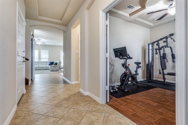 exercise room featuring ceiling fan, light tile patterned floors, and a tray ceiling