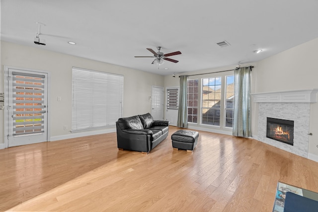 living room featuring ceiling fan, a stone fireplace, and light hardwood / wood-style floors