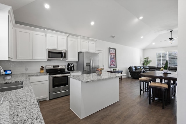 kitchen with lofted ceiling, light stone counters, a kitchen island, stainless steel appliances, and white cabinets